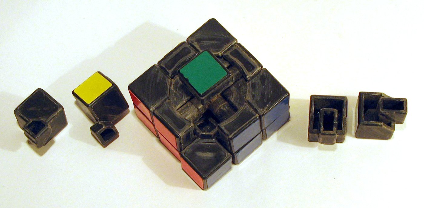 Cubo de Rubik clásico con una arista, una esquina y otras piezas sueltas al costado, que dejan ver el mecanismo interno